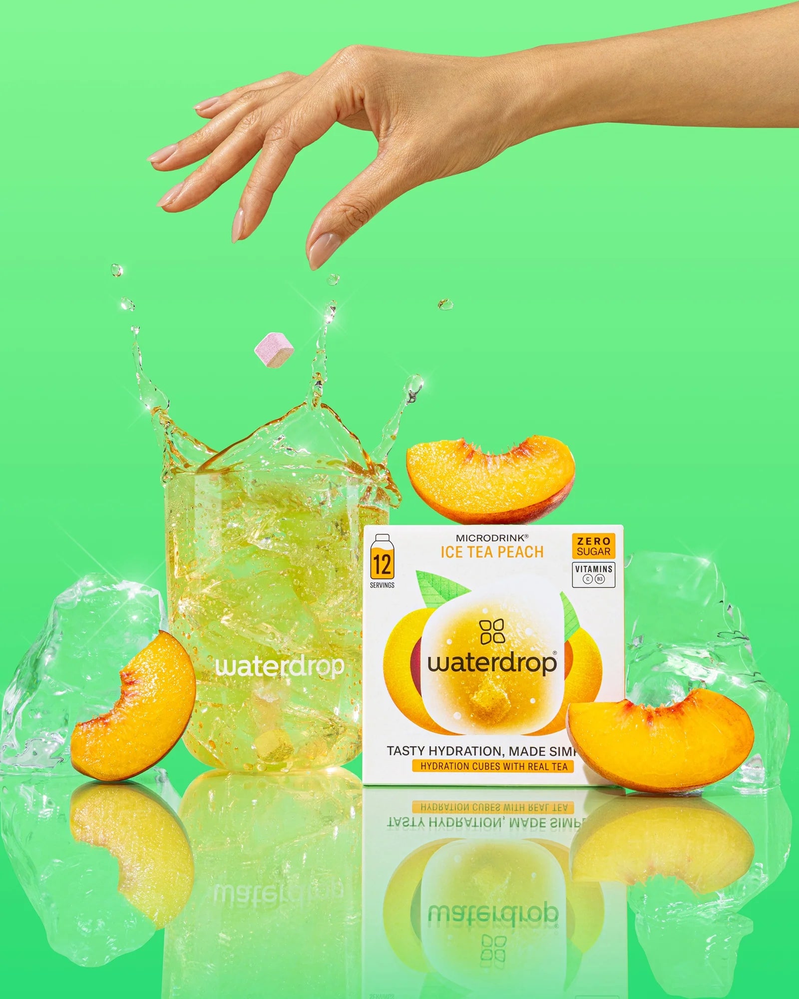Waterdrop logóval ellátott pohár őszibarackos jeges teával, jégkockákkal és kifröccsenő folyadékkal, őszibarack szeletekkel és egy Microdrink Ice Tea Peach dobozzal, 12 adaggal, zöld háttéren.