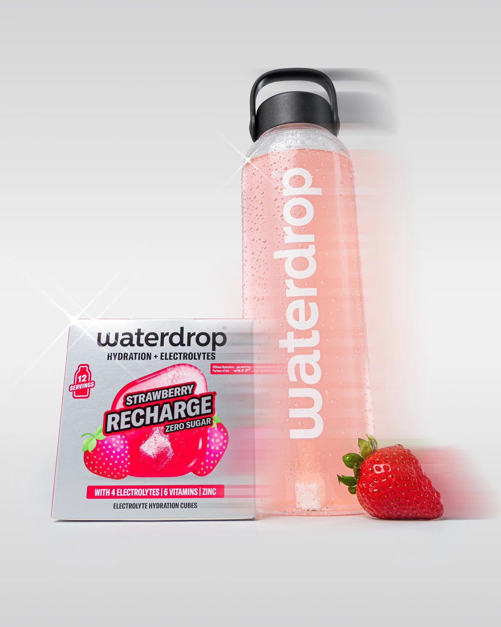 Újrahasználható waterdrop palack rózsaszín itallal, mellette egy cukormentes Strawberry Recharge doboz 12 adaggal és egy friss eper, fehér háttéren.