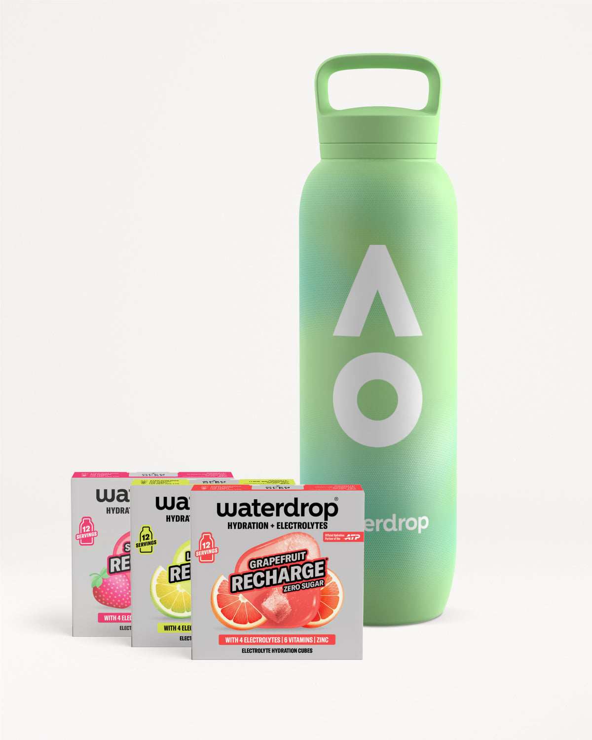 Zöld waterdrop újrahasználható palack fogantyús kupakkal, mellette három cukormentes Recharge doboz Strawberry, Lemon-Mint és Grapefruit ízben, dobozonként 12 adaggal, fehér háttéren.