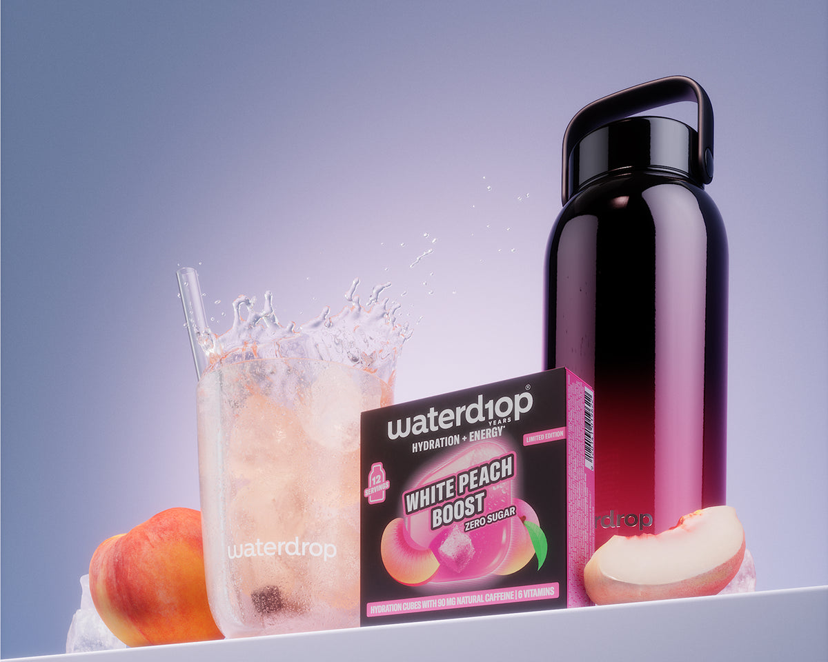 A White Peach Boost termék doboza jéghideg ital mellett fekete újrahasznosítható üveg van fehér polcon.