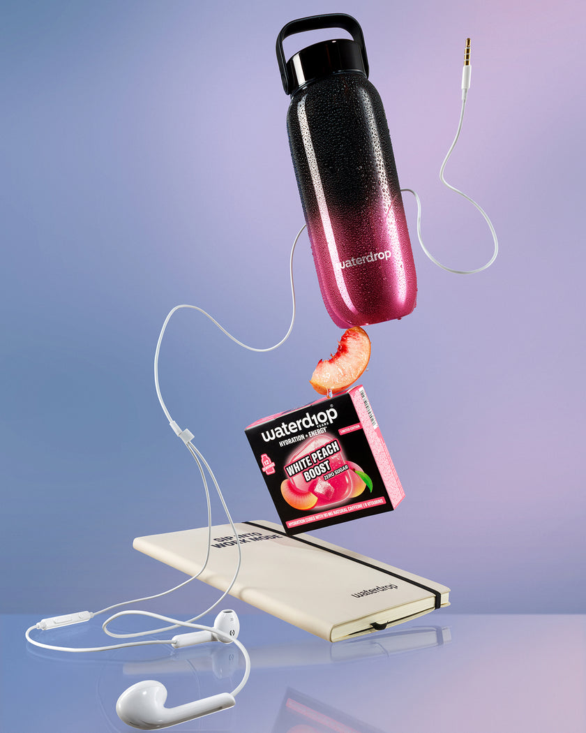 Egy fekete-porózán átmenetet tartalmazó víz-kanna fehér powerbank felett lebeg, fehér vezetékekkel összekötve, közelében egy barackdarab.
