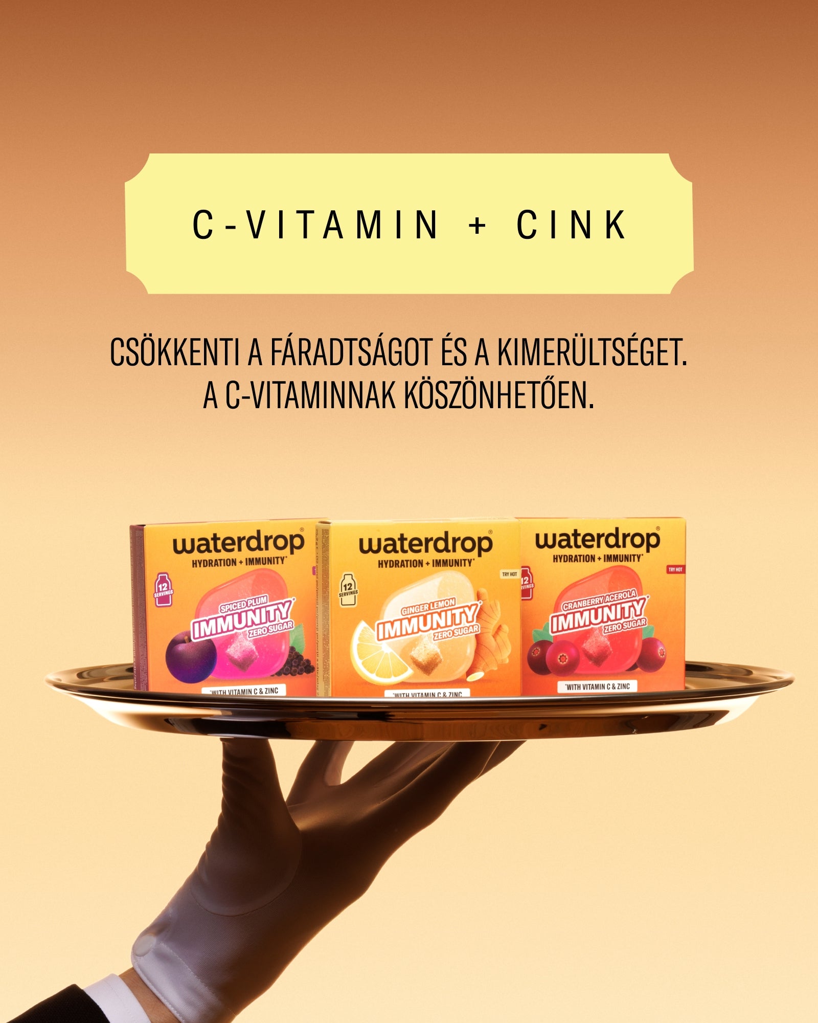 Kéz tart egy tálcát három Waterdrop C-vitamin termékcsomaggal meleg narancssárga háttér előtt.